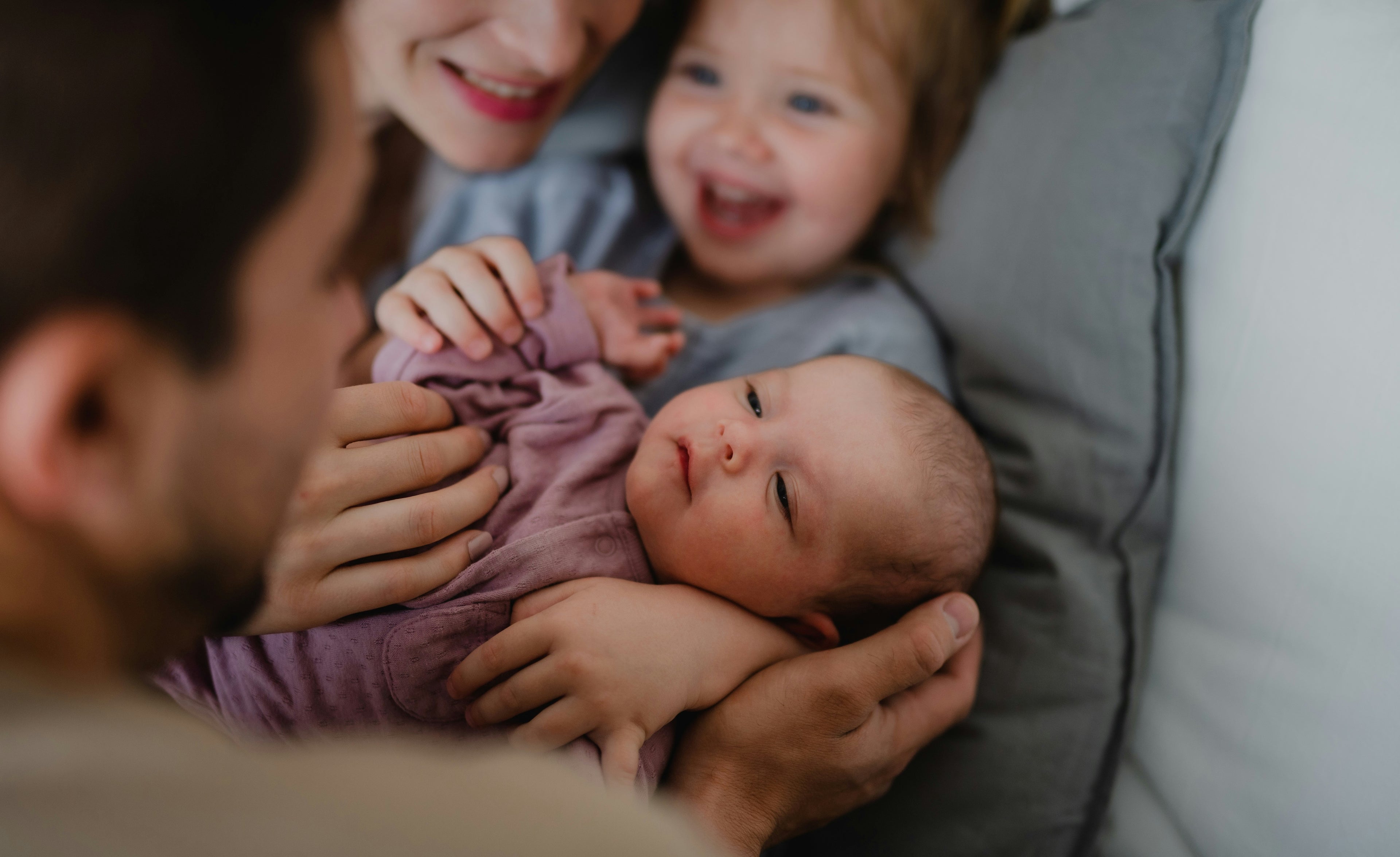 Newborn baby held by a couple with a toddler in the background